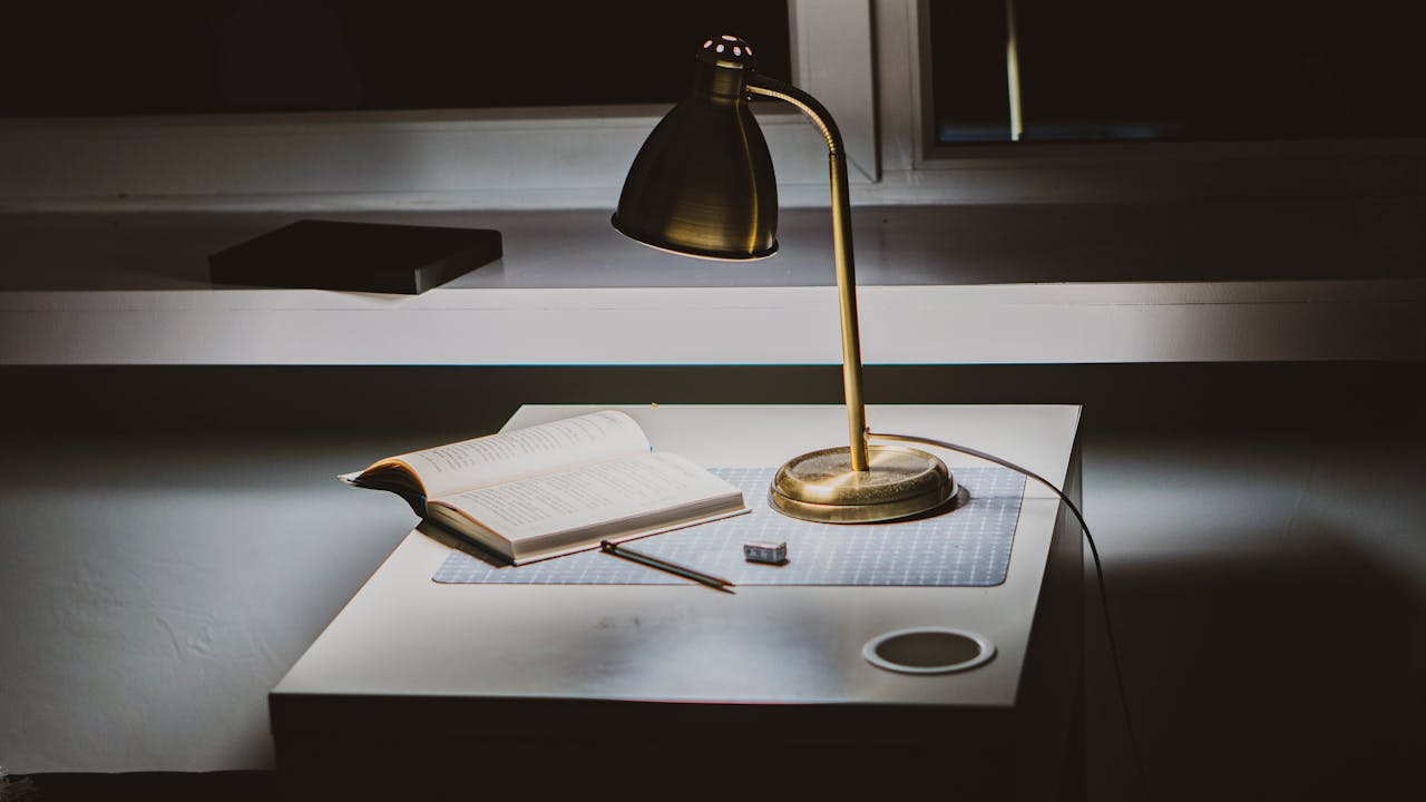 A warm, inviting study space featuring a lamp, open book, and writing utensil on a modern desk.