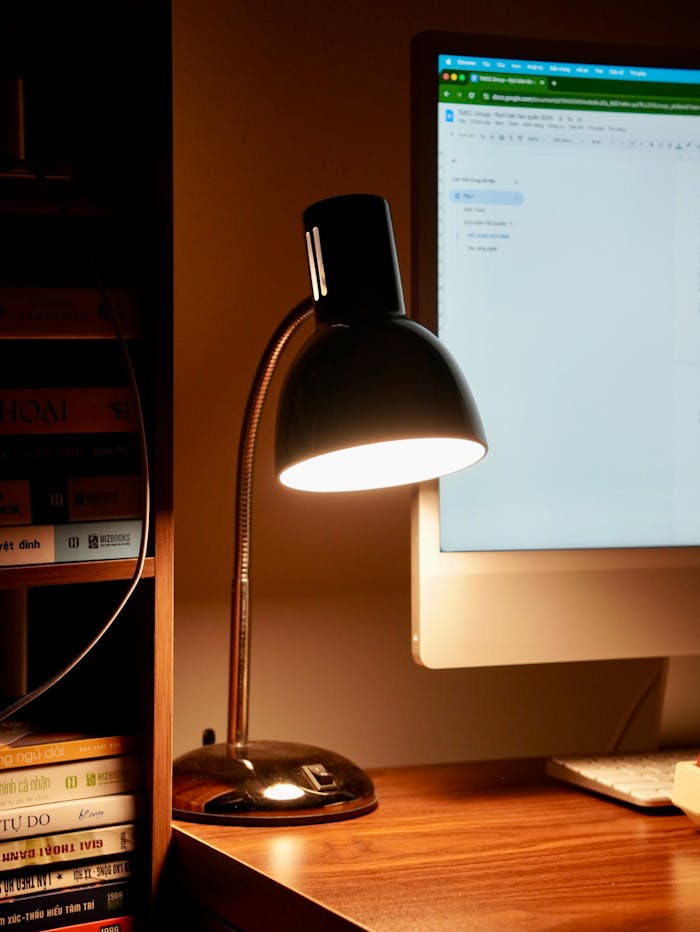 Warmly lit home office with desk lamp, books, and computer screen.