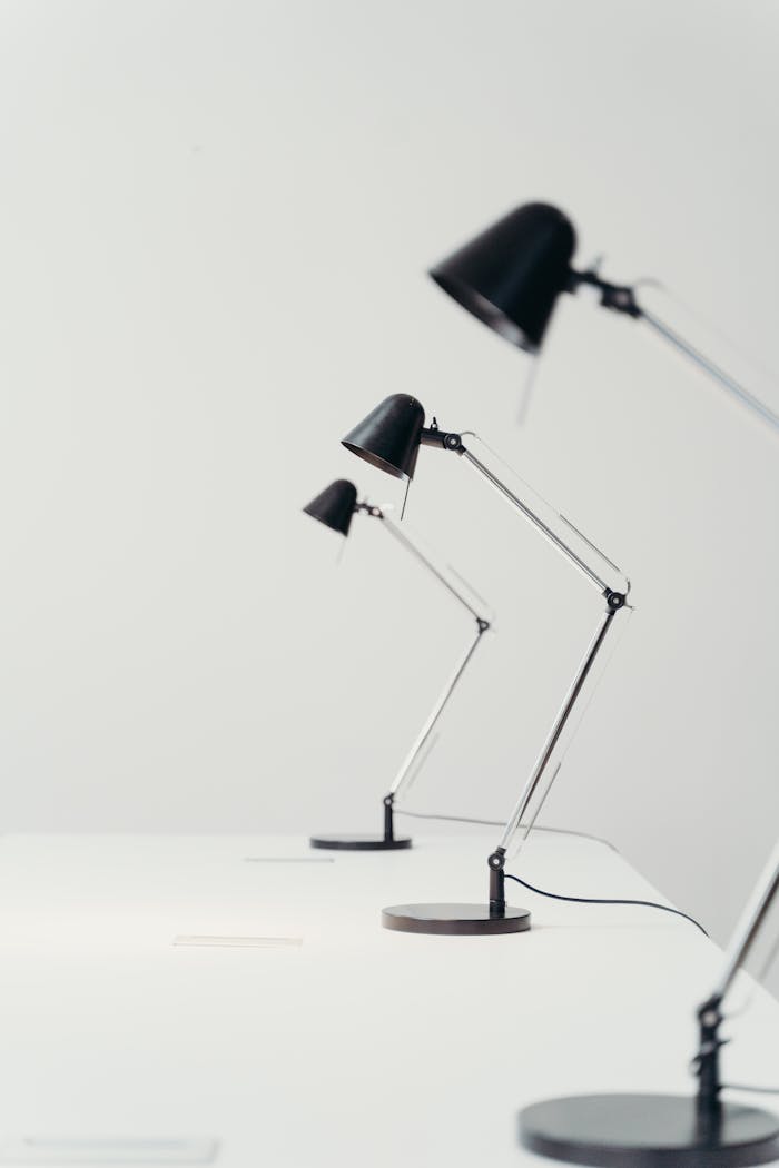Three sleek metal desk lamps arranged in a row on a clean white table, showcasing minimalist design.